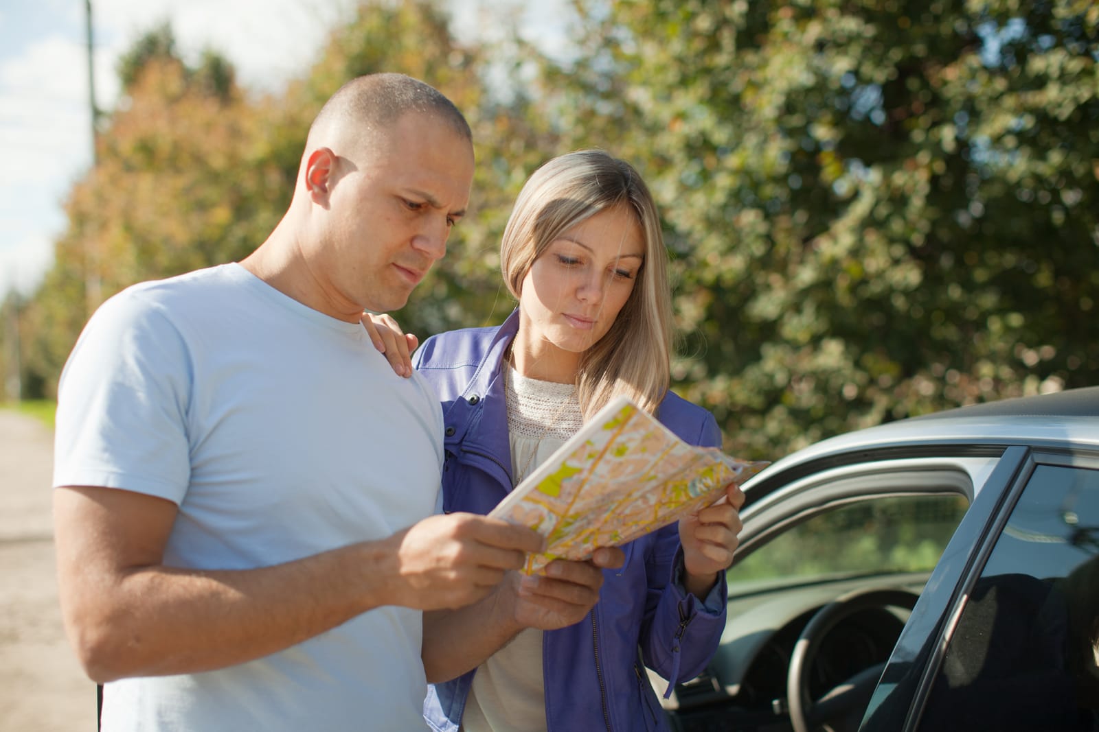 Couple reviewing a map by their car, planning a move, preparing for travel, and navigating a new destination.