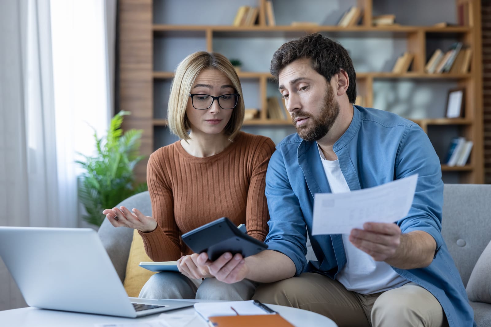 Couple reviewing rental documents and financial information together at home with a laptop, calculator, and paperwork.